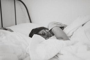 Grayscale photo of sleeping woman lying on bed exhausted. Needing chronic fatigue syndrome treatment