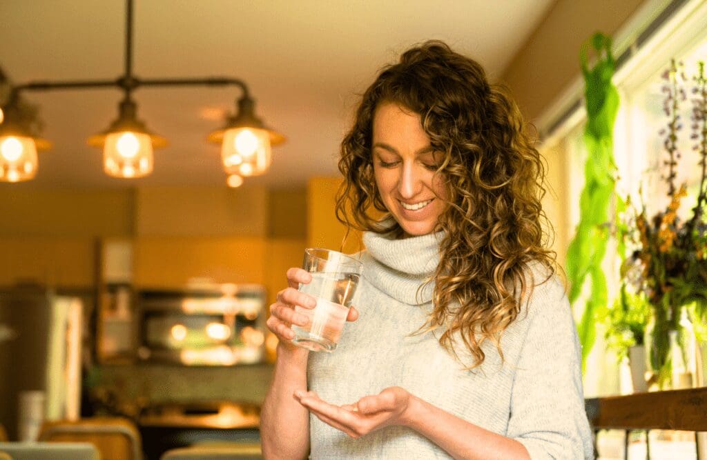Woman holding a glass of water and a supplement on her palm. Successful Detox. Clinical Nutrients. Brisbane Livewell Clinic How Long Does It Take to Detox Heavy Metals from the Body?