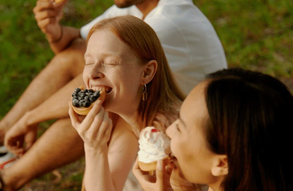 Friends sitting on the grass, eating pastries. Hypnotherapy for Weight Loss Near Me. Food Allergy Testing. Brisbane Livewell Clinic