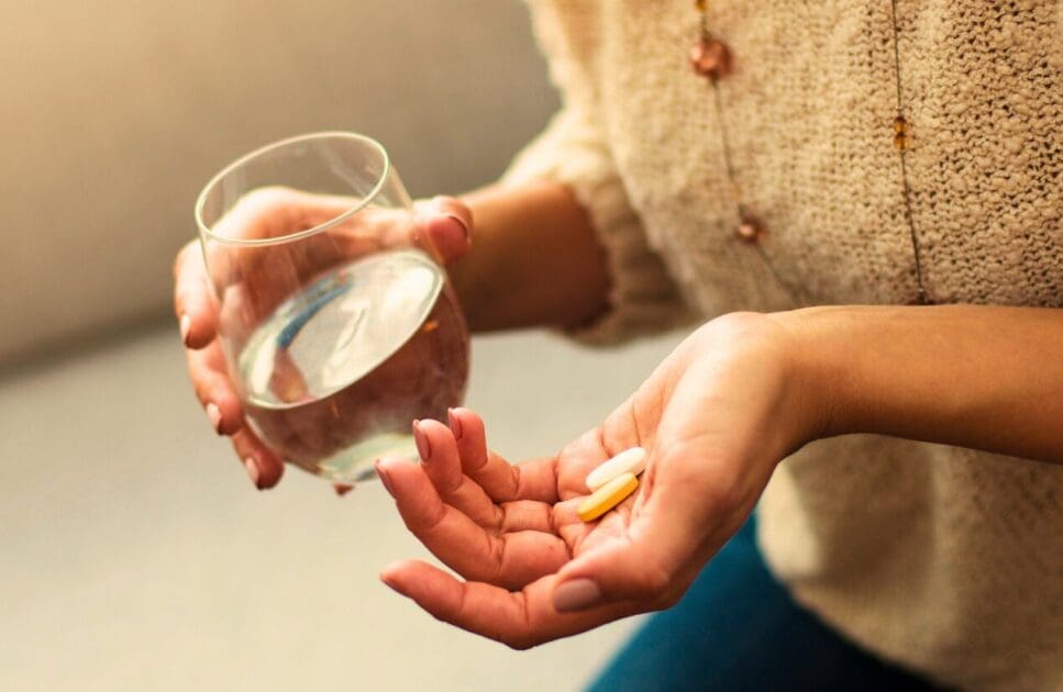 Woman holding a glass of water and vitamins. Happy Menopause. Brisbane Livewell Clinic