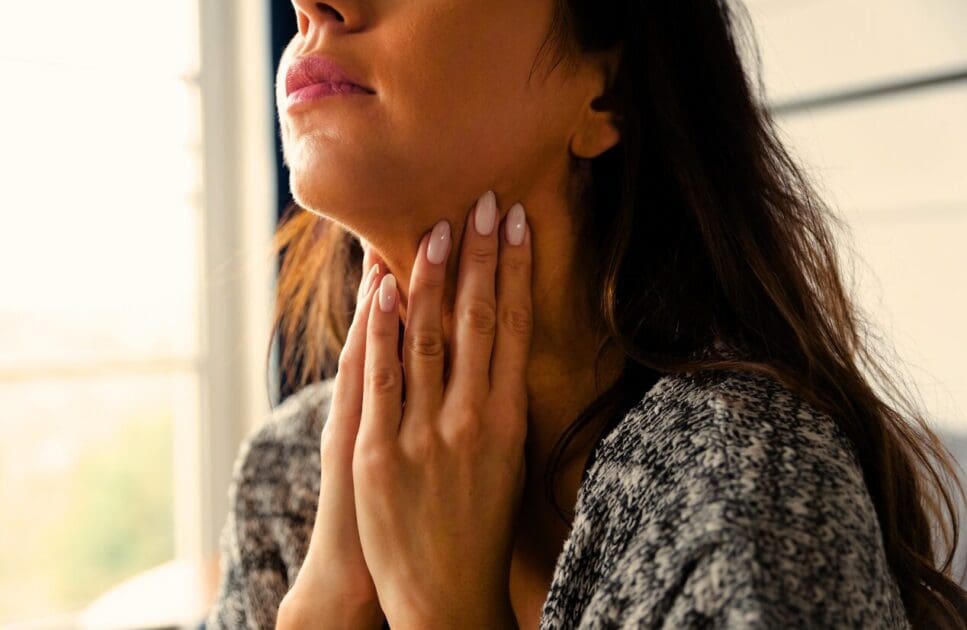 Close-up of a woman touching her throat with both hands. Thyroid Health. Brisbane Livewell Clinic. Hyperthyroidism