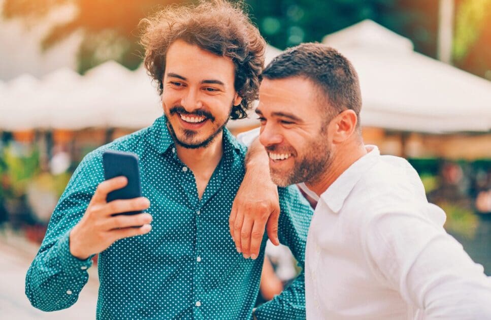 Two male friends looking at a smartphone. Addiction Hypnotherapy. Acupuncture for Migraines. Brisbane Livewell Clinic