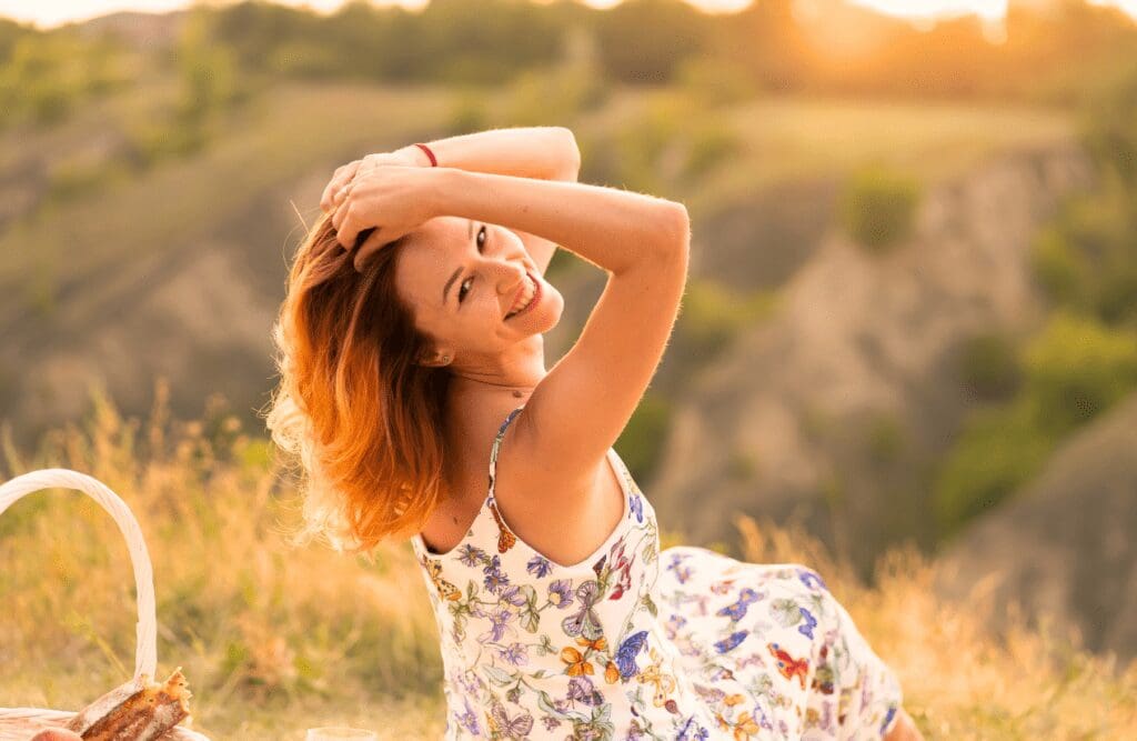Happy woman sitting on the grassland while enjoying the sunset. Hypnotherapy FAQs. Migraine. Osteopathy for Scoliosis and Spinal Curvature. Osteopath. Brisbane Livewell Clinic
