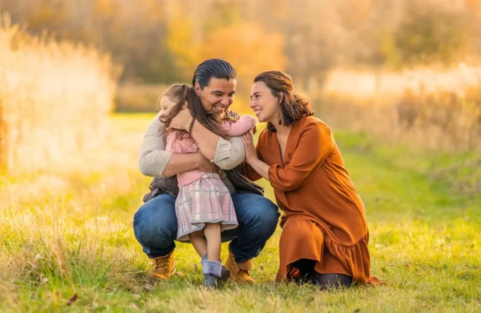 Little girl hugs her mom and das as they kneel down on the grass. Marriage Counselling Brisbane. Brisbane Livewell Clinic