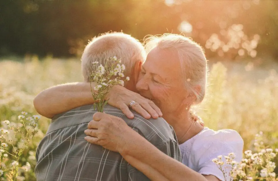 Couple sharing a warm hug in a field filled with flowers. Hypnotherapy near Nundah. Marriage Counselling Near Me. Osteopathy and Ageing. Brisbane Livewell Clinic
