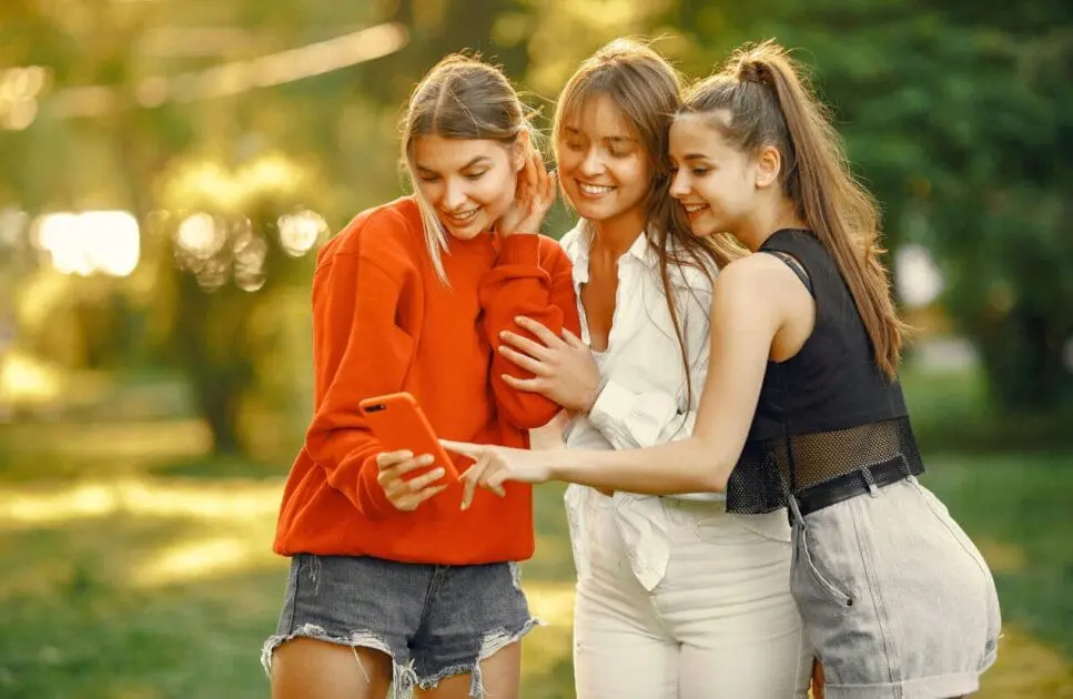 Three young women outdoors, smiling and looking at a smartphone. Counselling Tingalpa. Brisbane Livewell Clinic