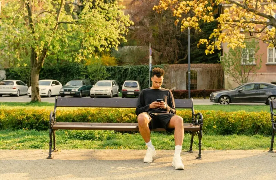 Man sitting on a bench, using his smartphone. Alcohol and Drug Counselling. Addiction Hypnotherapy. Osteopath for Sciatica. Osteopathy and Ankle or Foot Pain. Brisbane Livewell Clinic