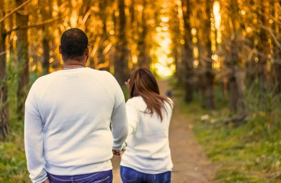 Couple walking hand in hand along a path surrounded by tall green trees. Hypnotherapy near Hendra. Brisbane Livewell Clinic