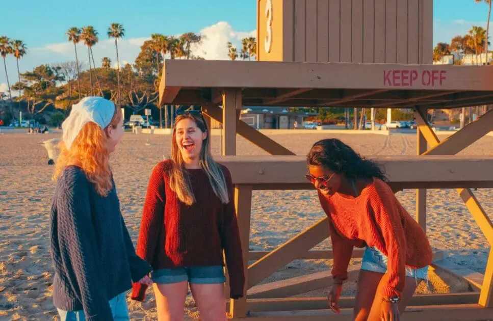 Three woman standing and laughing near the lifeguard tower. Hypnotherapy near Kedron. Naturopath Women's Health. Brisbane Livewell Clinic