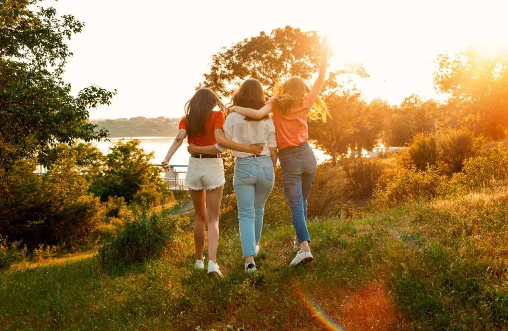 Three young women are walking together in a grassy field at sunset. Counselling Morningside. Counselling Norman Park. Brisbane Livewell Clinic