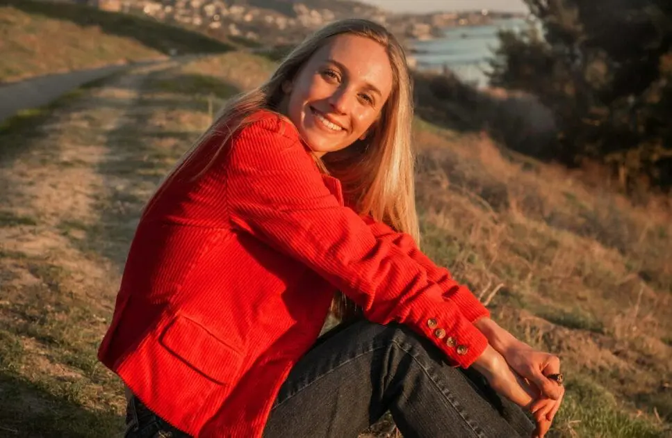 Smiling woman in a red jacket sitting on a hill. Hypnotherapy near Nundah. Holistic Counselling Brisbane. Brisbane Livewell Clinic