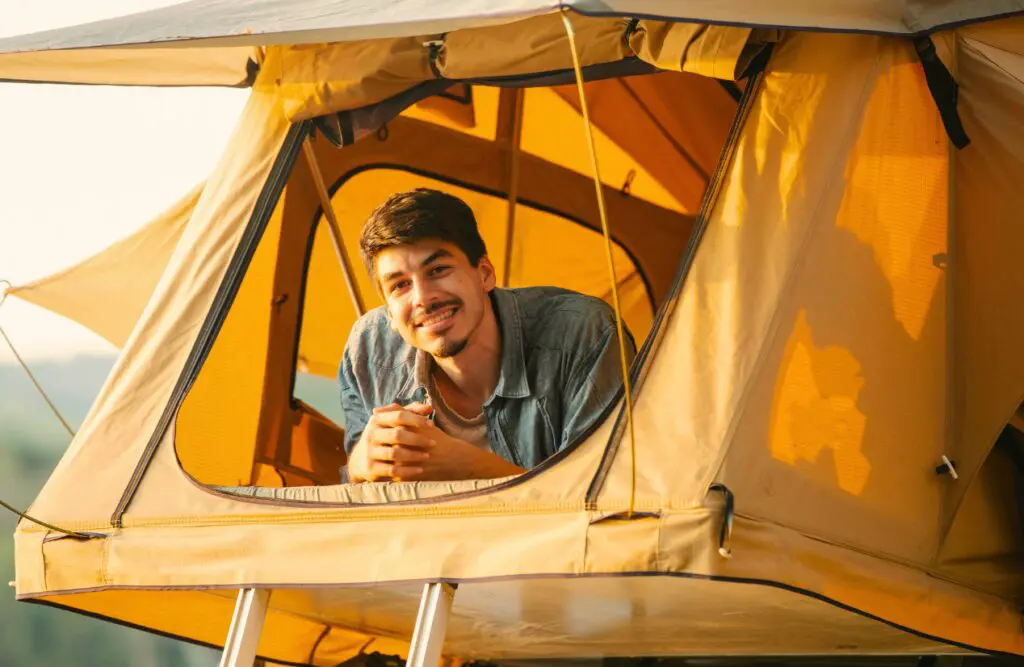 Young man smiling from a window of a rooftop tent. Naturopath vs Homeopath. Hypnotherapy for Alcohol Addiction. Osteopath for Frozen Shoulder. Brisbane Livewell Clinic